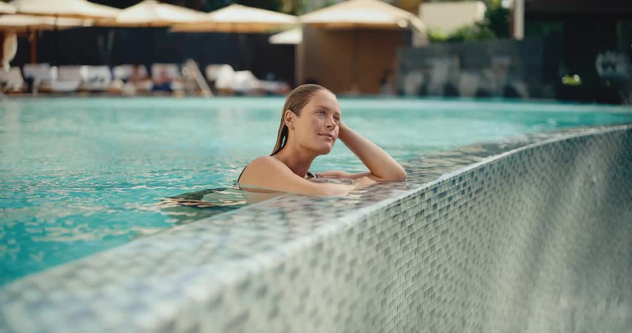 A tranquil woman enjoys a peaceful moment at the edge of a sparkling blue swimming pool at a luxury resort
