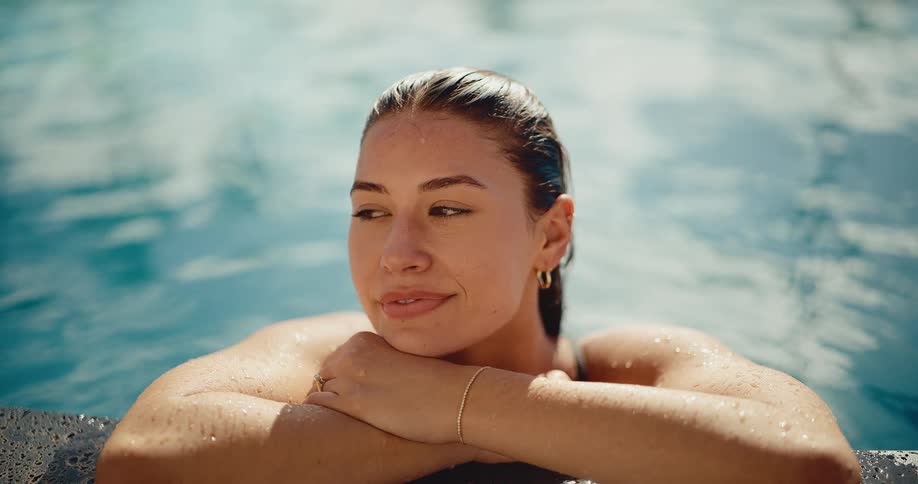 Close-up portrait of a serene young woman with wet hair smiling while relaxing in a swimming pool