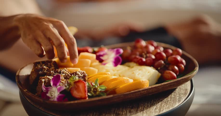 A person takes a piece of fresh cantaloupe from a beautiful tropical fruit and pastry platter during a relaxing morning