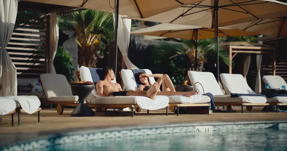 An attractive couple sunbathes and relaxes on luxurious lounge chairs by a resort swimming pool