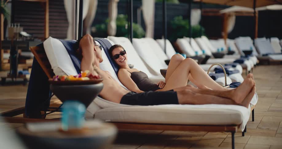 A happy couple in swimwear relaxes together on lounge chairs by the pool at a luxury resort