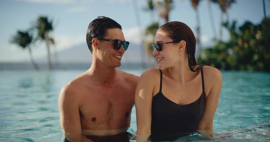 Happy attractive couple looks lovingly at each other while relaxing in a beautiful luxury resort swimming pool on vacation