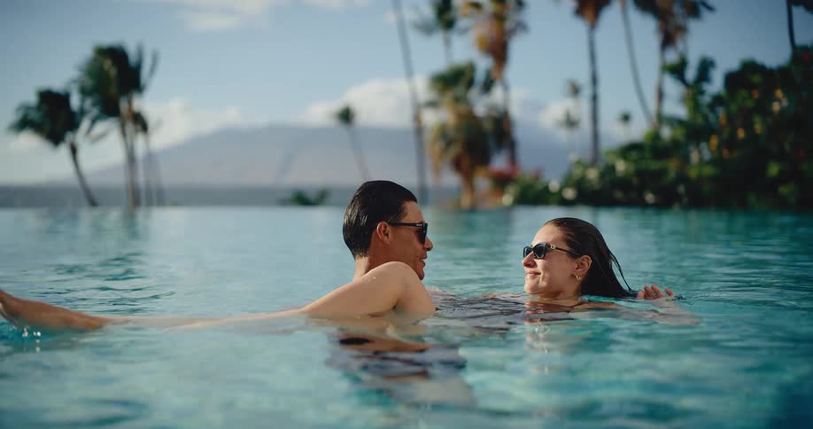Attractive romantic couple relaxes together in a beautiful infinity pool at a luxury tropical resort