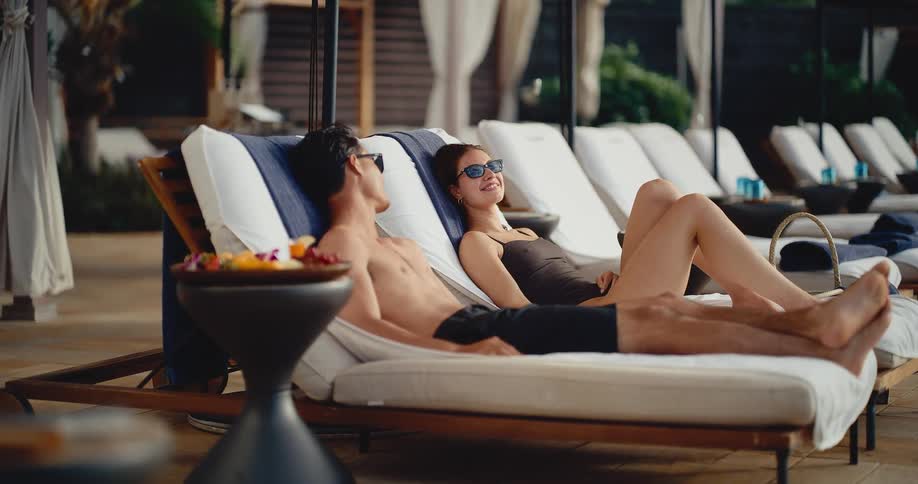 Young attractive couple enjoys their vacation while lounging by the pool at a luxury hotel