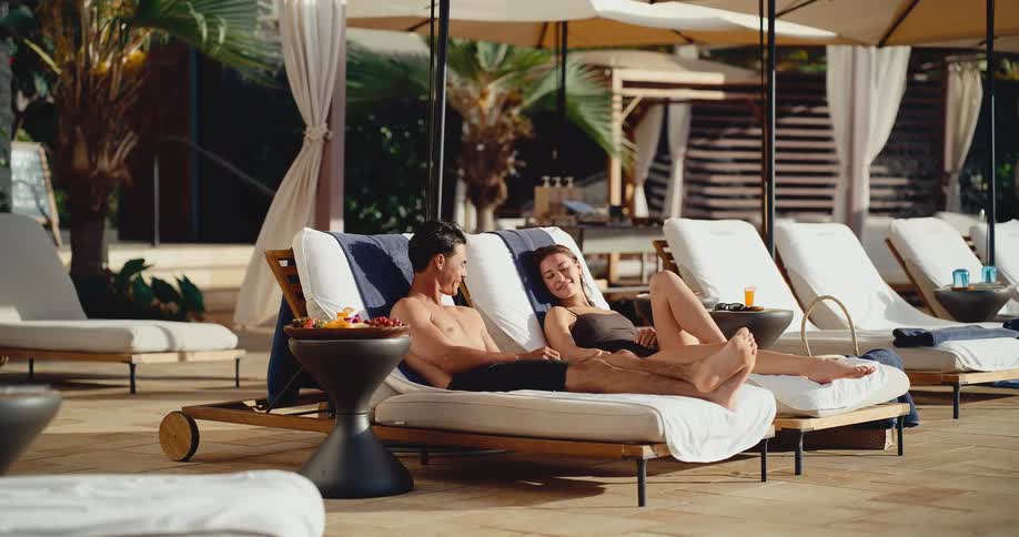 Happy couple relaxes on poolside lounge chairs, enjoying their vacation at a luxurious tropical resort