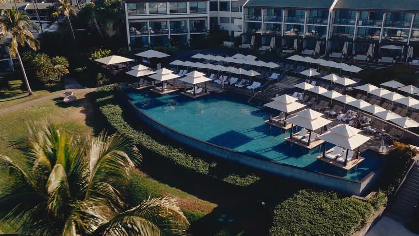 Aerial view of a luxury tropical resort pool with cabanas and lounge chairs on a sunny day