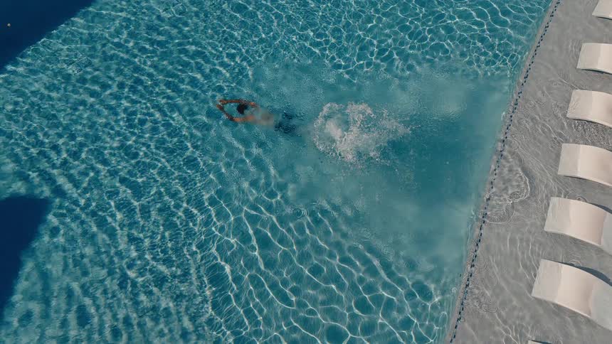 From above, a man dives gracefully into the shimmering blue water of a luxury swimming pool in slow motion