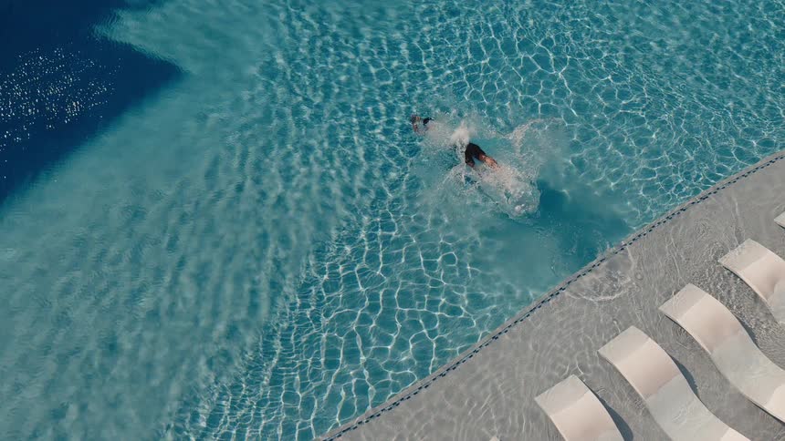 High angle slow motion shot of a man diving into a crystal clear blue swimming pool at a luxury resort