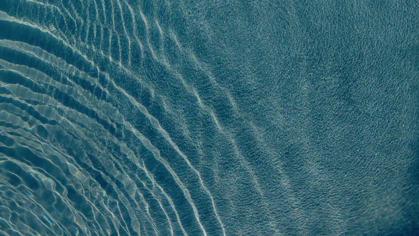 Abstract top-down shot of calm blue water with sunlight creating rippling patterns on the surface