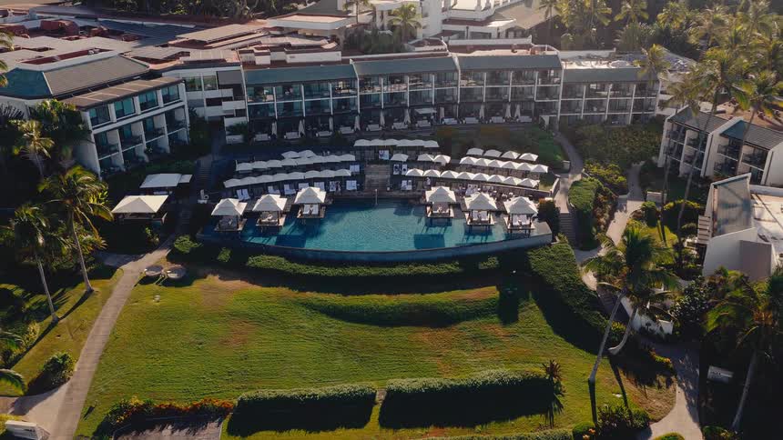 Aerial drone footage pulls back from a luxurious tropical resort pool with cabanas during a beautiful golden hour sunrise