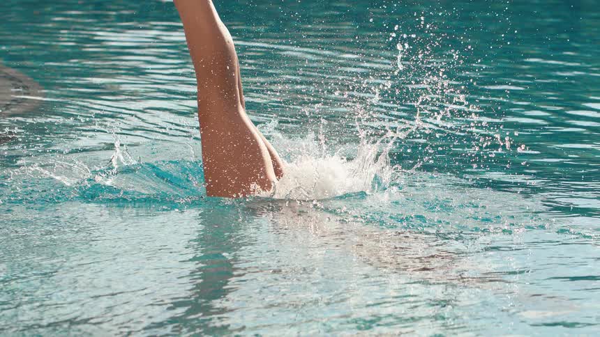 A woman in a black swimsuit gracefully dives into the clear blue water of a swimming pool in slow motion