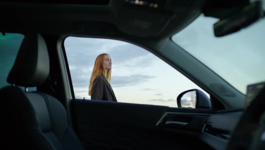 View from inside a modern car of a serene woman with long hair enjoying the peaceful twilight sky on her journey