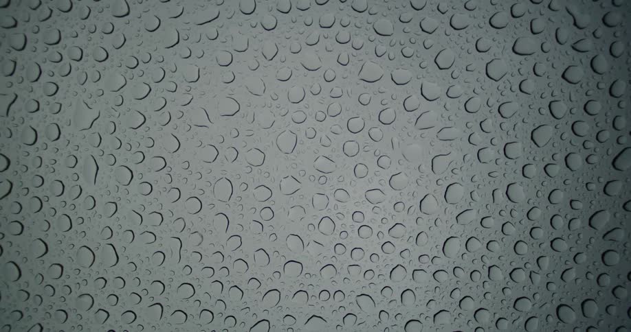 Static top-down view of water droplets from rain resting on a glass surface