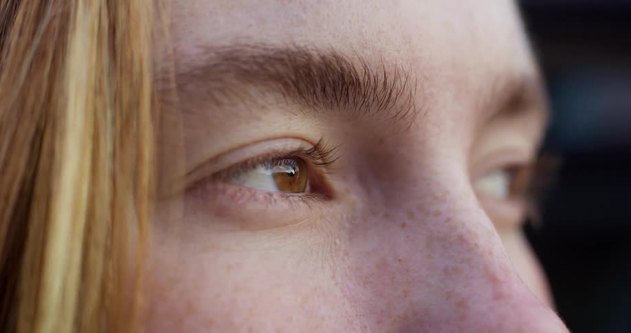 An extreme close-up macro shot captures the detail of a young person's brown eye and freckled skin as they look off-camera