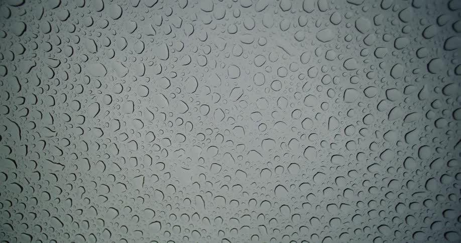 Abstract view looking up through a glass window covered in raindrops against a grey, overcast sky