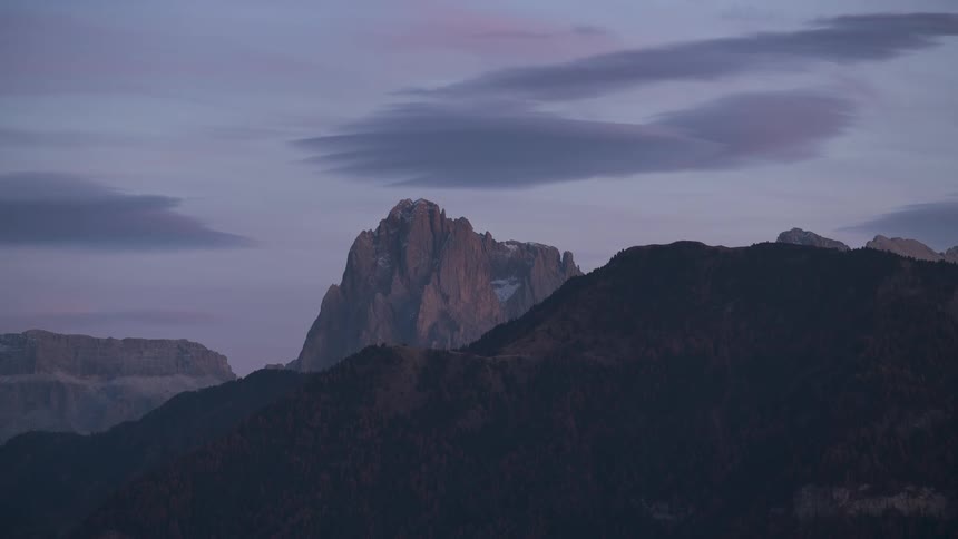 A serene view of the majestic Dolomite mountains at twilight as soft clouds drift overhead