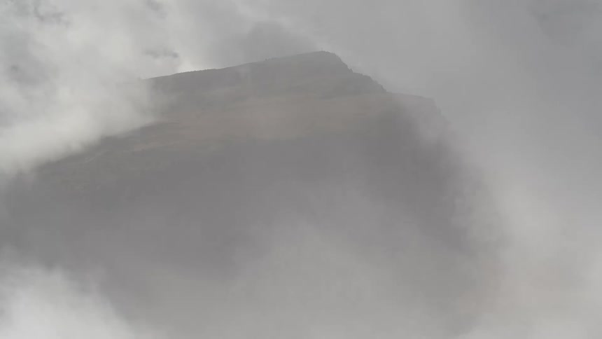 A dramatic time-lapse of a mountain peak being revealed and then obscured by thick, fast-moving clouds