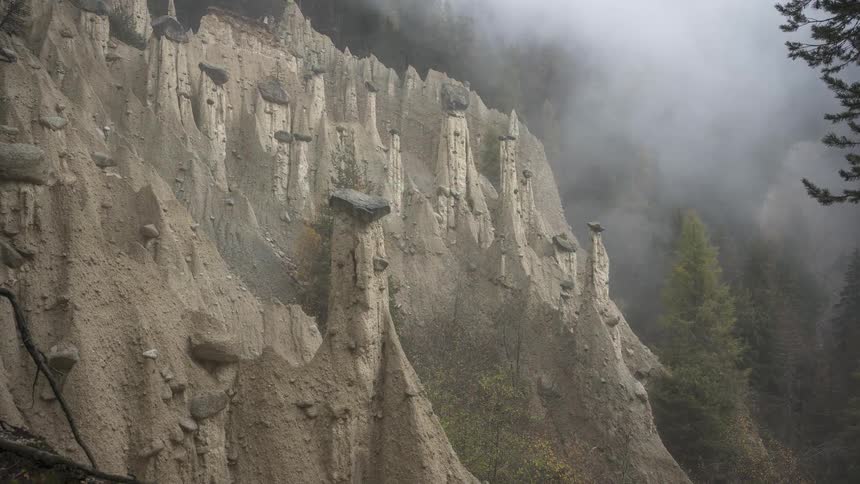 A slow zoom-out reveals the mystical earth pyramids of Perca emerging from a foggy mountain forest