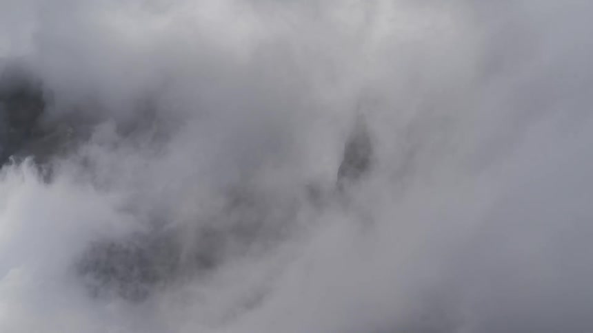 A dramatic time-lapse shows majestic rocky mountain peaks being completely enveloped by a thick blanket of fog