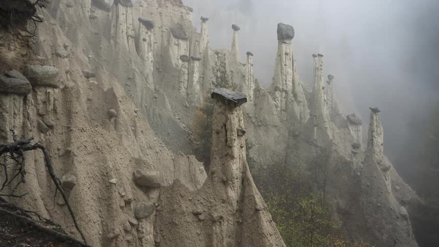 A slow zoom out reveals the unique earth pyramid rock formations of Euseigne, Switzerland on a moody, foggy day