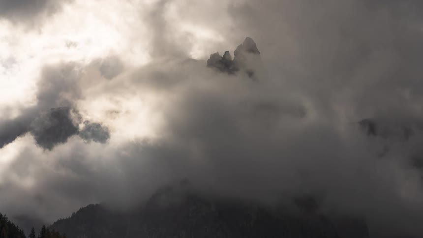 Time-lapse of dramatic, moody clouds slowly parting to reveal a majestic mountain peak