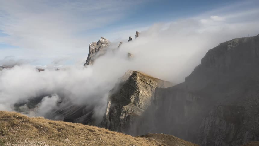 A time-lapse of dense fog rolling over majestic, rugged mountain peaks on a sunny day