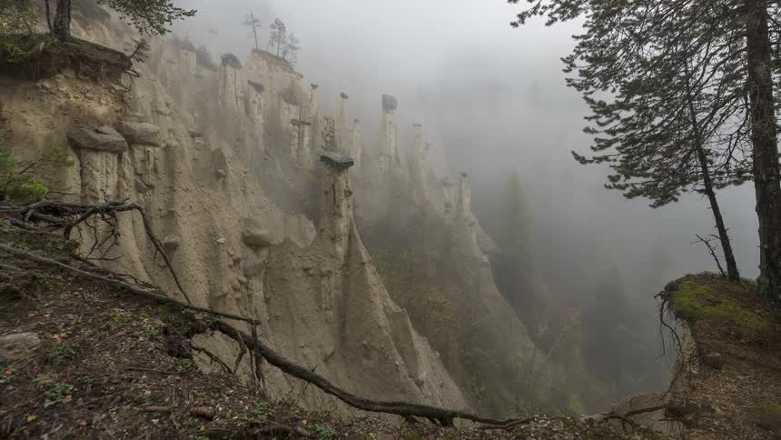 A mysterious timelapse of thick fog rolling over unique earth pyramid hoodoos in a forest valley