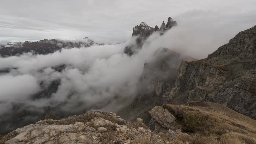 A dramatic view of the jagged Seceda mountain peaks as clouds and fog drift through the surrounding valley