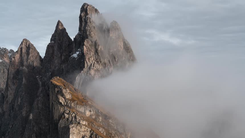 A time-lapse of majestic jagged mountain peaks as dense clouds roll in and cover the rugged landscape