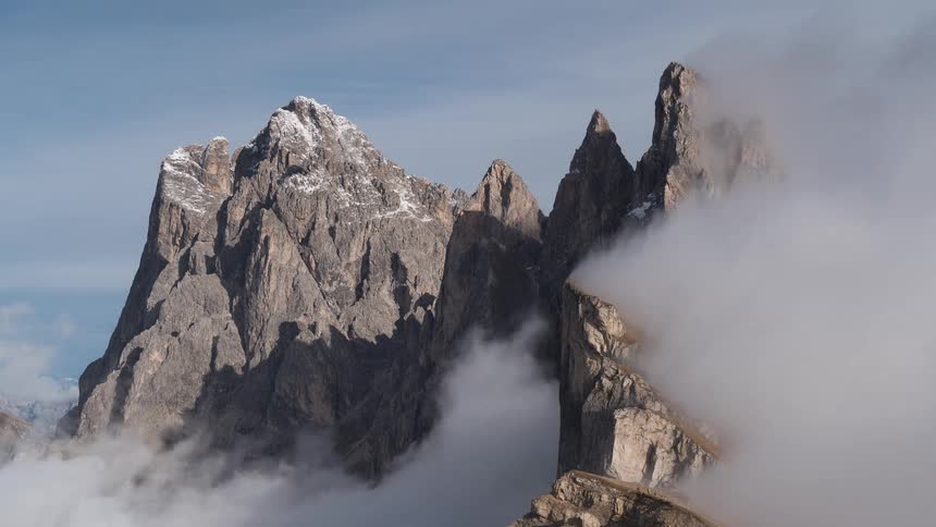 Dramatic clouds swirl around the jagged, snow-dusted peaks of the Dolomites mountains