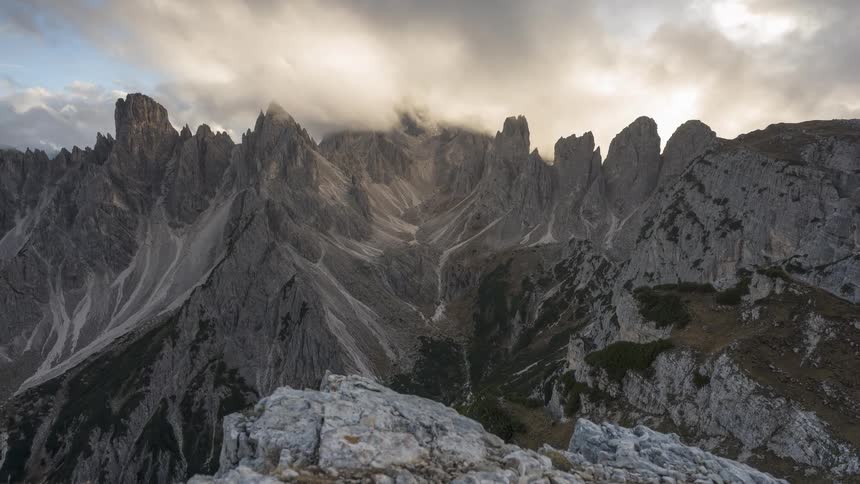 A dramatic dolly-out timelapse captures clouds moving over the jagged peaks of the Cadini di Misurina mountain range in the Dolomites at sunrise