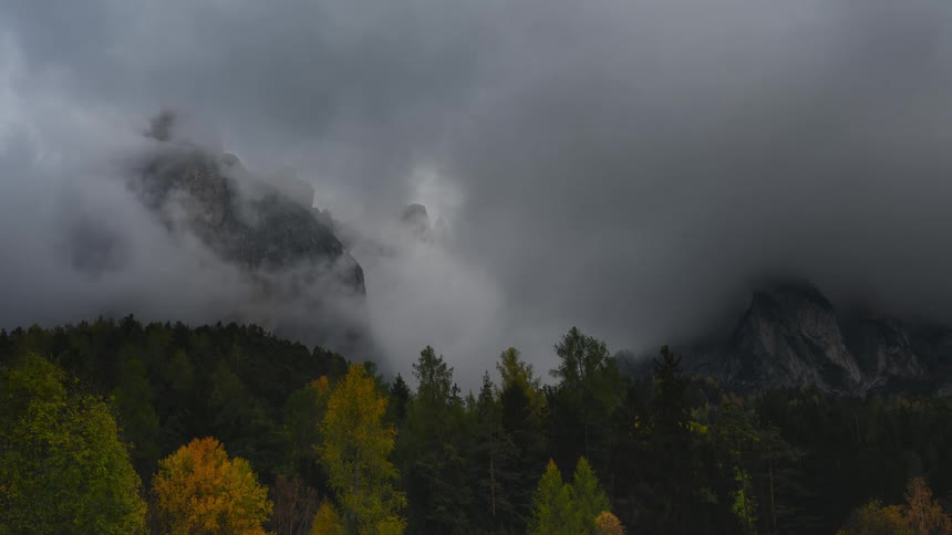 Timelapse of dramatic dark storm clouds rolling over a mountain range and colorful autumn forest