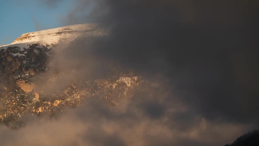 A dramatic timelapse captures clouds rolling over a majestic snow-capped mountain peak at sunset