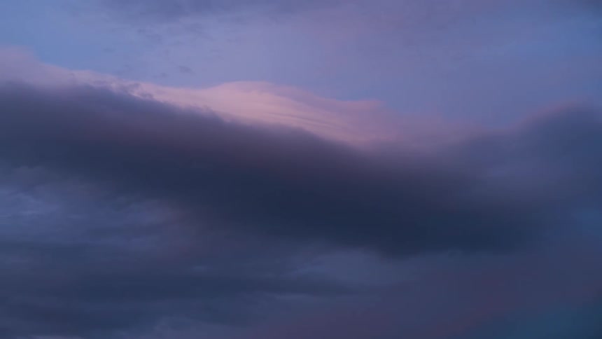 A serene view of dark purple and pink clouds slowly drifting across the sky at dusk
