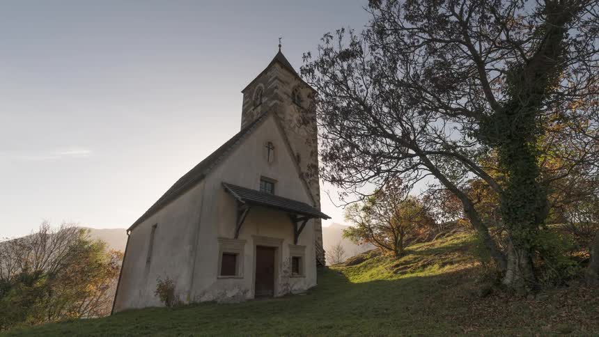The sun rises over a quaint, ancient church on a verdant hillside in this stunning daybreak timelapse