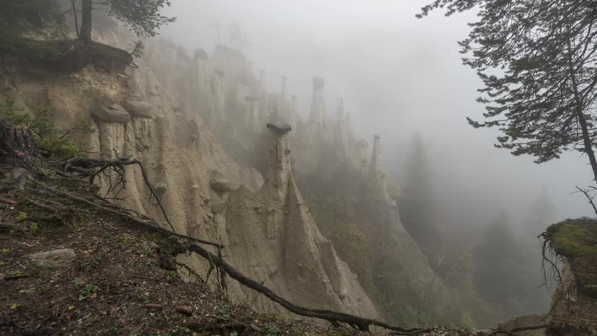 A mysterious timelapse of thick fog rolling over and obscuring unique hoodoo rock formations in a mountain forest