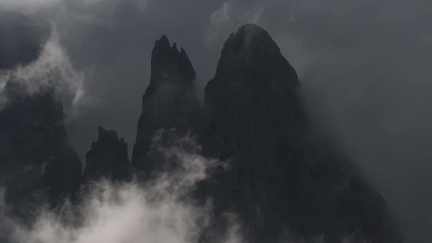 Time-lapse of ominous grey clouds swirling around and completely obscuring dark mountain peaks
