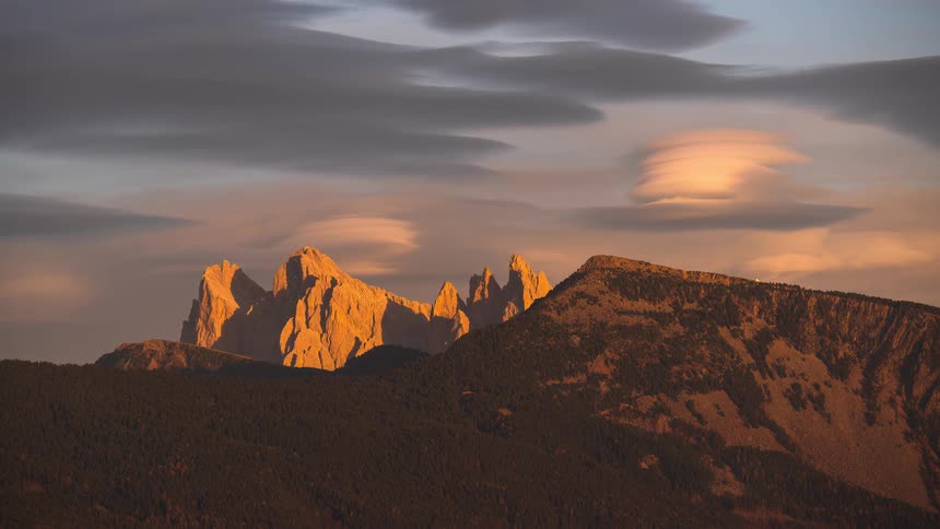 A breathtaking timelapse captures the golden hour light fading into a colorful alpenglow sunset over the jagged peaks of the Dolomites