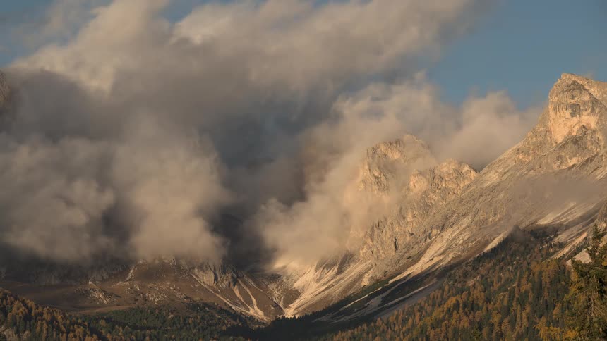 Clouds drift slowly through a rugged mountain valley in the Dolomites, illuminated by the warm light of sunrise