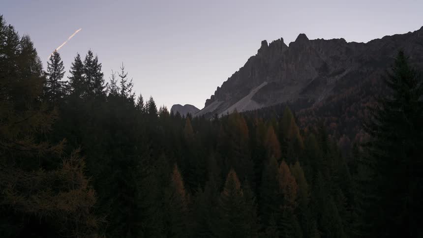 A serene timelapse captures the transition from predawn to sunrise over a rugged mountain peak and a dense alpine forest