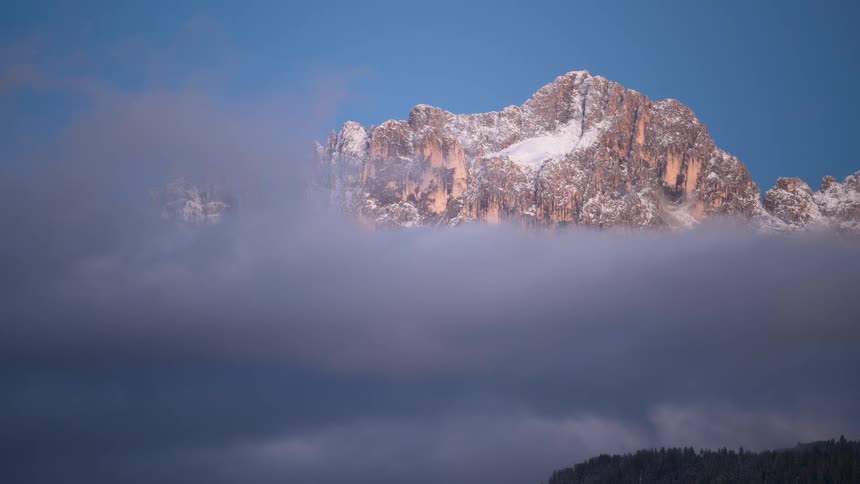 A stunning time-lapse as clouds clear to reveal majestic snow-capped mountain peaks illuminated by the morning sun