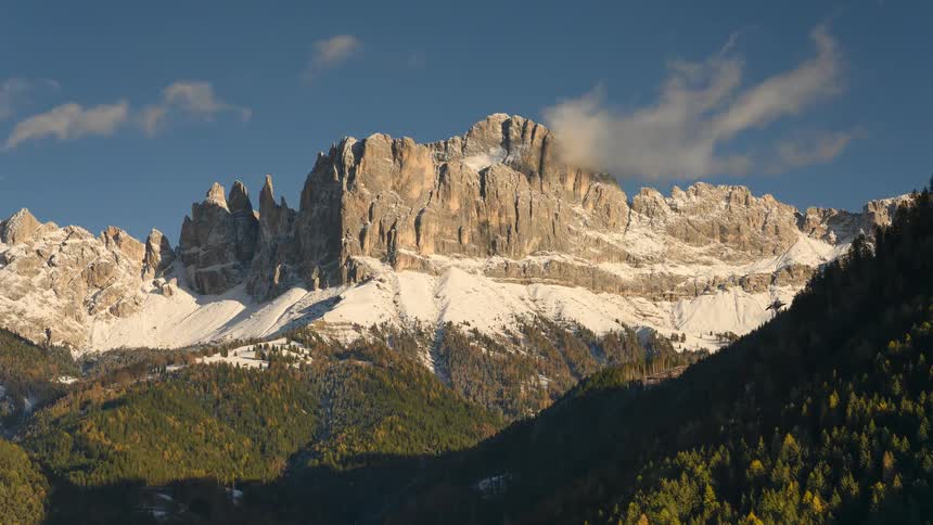 A slow zoom-out timelapse captures the breathtaking beauty of the sunlit and snow-dusted Sella Group mountain range in the Dolomites on a clear day
