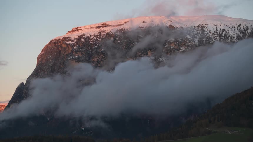 A time-lapse of rosy clouds revealing a majestic, snow-capped mountain peak during a beautiful sunset