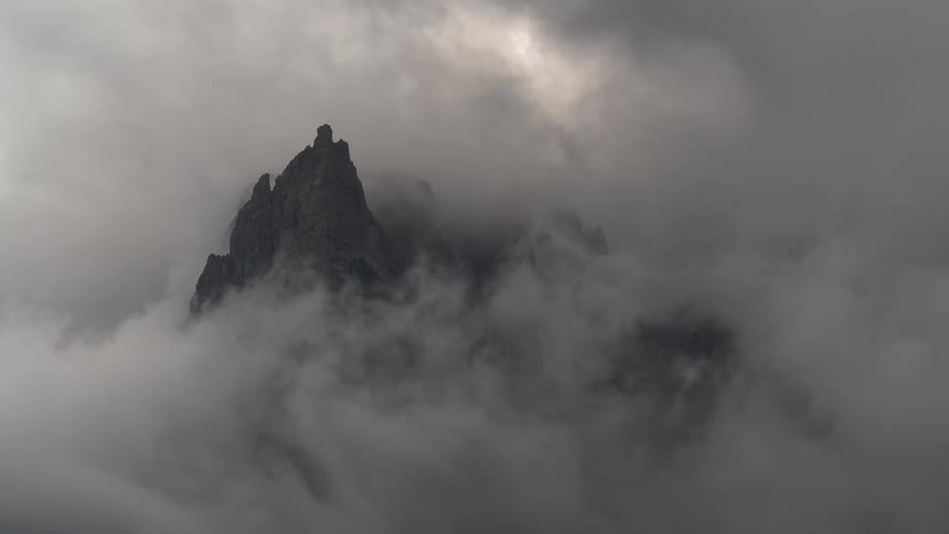 A dramatic and moody time-lapse reveals jagged mountain peaks through swirling dark clouds