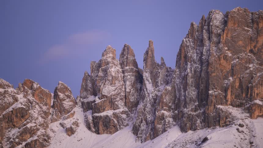 A beautiful timelapse shows the sky changing from purple dawn to blue morning over majestic, snow-covered mountains
