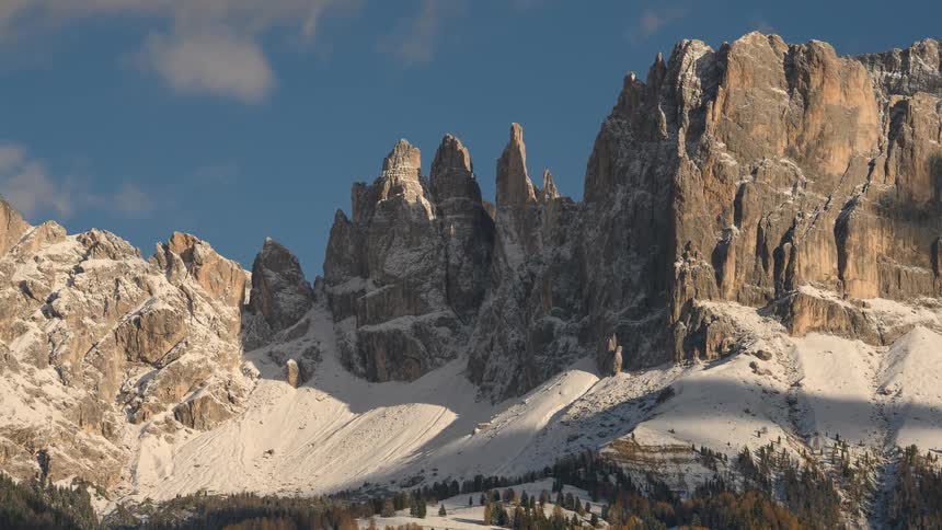 A stunning timelapse captures the play of light and shadow across the majestic, snow-dusted peaks of the Dolomites under a clear blue sky