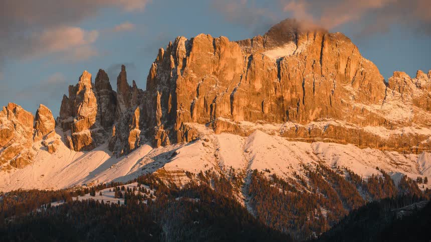 Timelapse of a stunning sunset casting a golden glow over snow-covered Dolomite mountains before fading into twilight