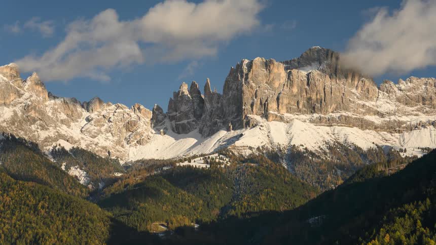 An aerial pan across a stunning snow-capped mountain range above a verdant forest on a clear day