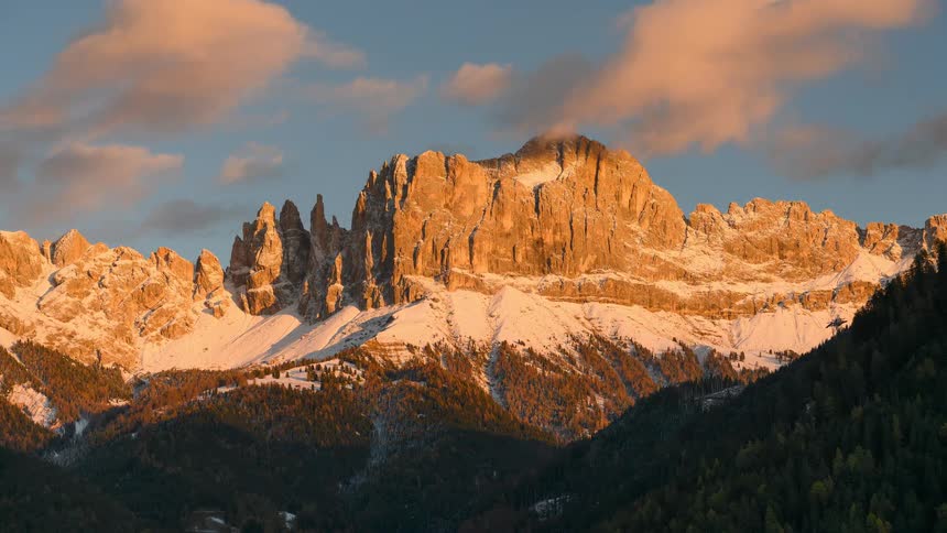 A stunning timelapse of the sunset casting a beautiful golden and pink glow on the snow-covered Dolomite mountains in Italy