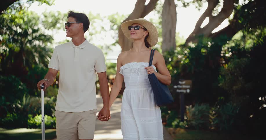 Stylish couple holding hands and walking with their luggage after arriving at a tropical luxury resort for their vacation